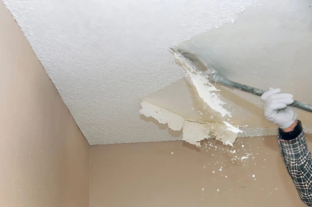 A professional painter removing popcorn ceiling with special tools